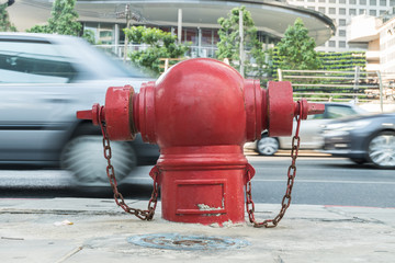 red fireplug standing alone on footpath/motion blur car backgrou
