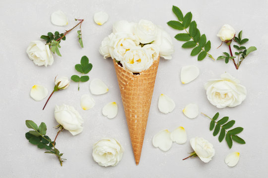 Ice cream of rose flowers in waffle cone on light gray background from above, beautiful floral decoration, vintage color, flat lay styling