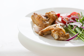 Homemade tasty roasted chicken wings with vegetables on a white plate, closeup