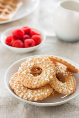 Cookies with sugar drops on a white plate with raspberries on a background on a linen textile, closeup