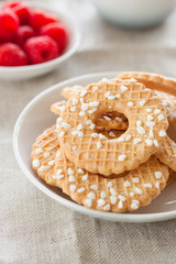 Cookies with sugar drops on a white plate with raspberries on a background on a linen textile, closeup