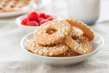 Cookies with sugar drops on a white plate with raspberries on a background on a linen textile, closeup