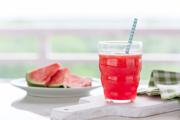 Homemade juicy cold drink with watermelon and water in a glass with blue straw on a wooden cut board