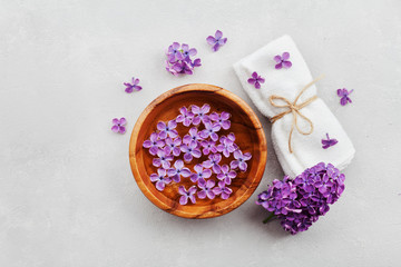 Obraz na płótnie Canvas Spa and wellness composition with perfumed lilac flowers water in wooden bowl and terry towel on gray stone background, aromatherapy, top view, flat lay