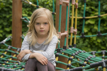 Portrait of Happy little blond girl playing on a rope web playground outdoor