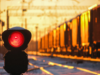 Railway traffic light at sunset shows red signal on railway. Red light. Moving train on the...