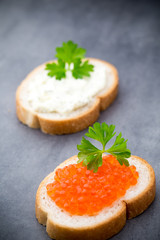 Bread with fresh cream cheese and red caviar on table.