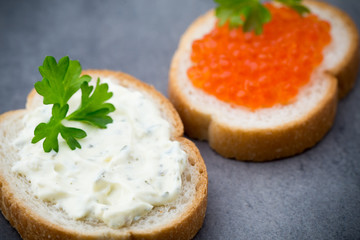 Bread with fresh cream cheese and red caviar on table.
