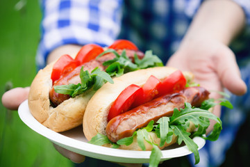 Hands holding grilled sausage sandwiches