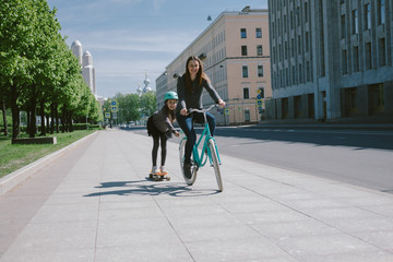 Mother and daughter ride a scooter and bicycle together