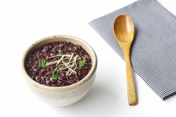 gruel (dark violet rice) with ginger and coriander in ceramic bowl and wooden spoon on napery isolated on white background