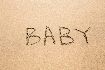 written word BABY on sand of beach