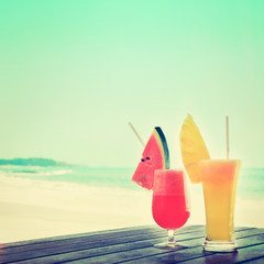 Colorful tropical fruit smoothies on wood table at the beach, vintage tone