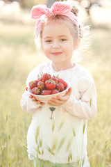 Smiling child girl 4-5 year old eating strawberry outdoors. Looking at camera. Summer season.