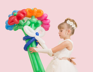 little girl with balloons in a ball gown isolated on a pink background
