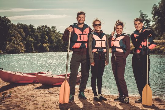 Cheerful friends having fun near kayaks on a beach.