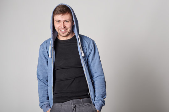 Handsome young man with light beard in blue hoodie,  on gray background
