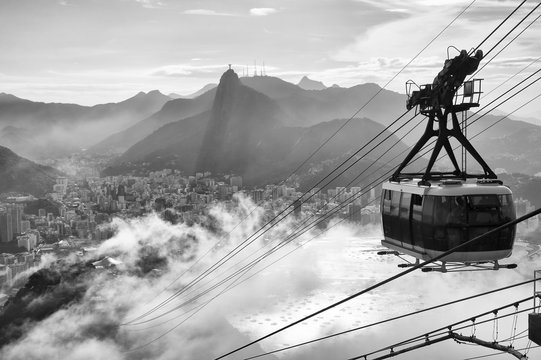 Black and white view of the misty city skyline of Rio de Janeiro, Brazil with a Sugarloaf (Pao de Acucar) Mountain cable car passing in the foreground