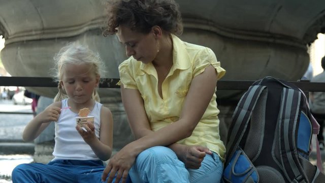 Mamma mangia gelato con bambina dai capelli biondi seduta su una fontana  a Roma, Italia, Europa