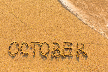 October - inscription on sand beach with the soft wave.