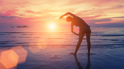 Female silhouette performs physical exercises on the beach after sunset.