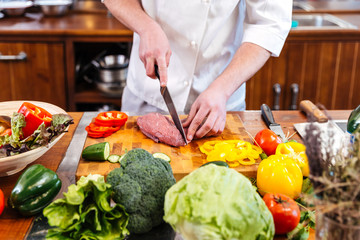 Professional chef cook cutting uncooked meat and fresh vegetables