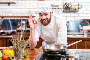 Cheerful bearded chef cook cooking and showing ok sign - obrazy, fototapety, plakaty