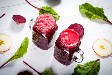 Red smoothies from beetroot, beet leaves and apple on white wooden table. Flat lay.