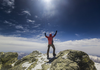 man standing on a cliff in mountains with hands up