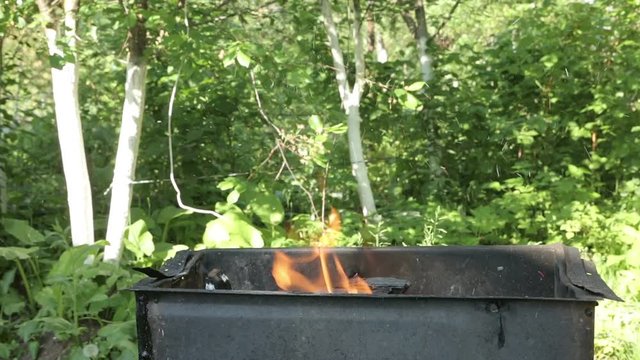 Men blows coals and fans embers in the barbecue bbq brazier. Outdoors picnic concept.