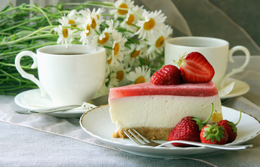 A piece of  cake, white cup of tea and strawberries..