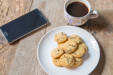 Chocolate chip cookies and coffee cup with smartphone, in morning time