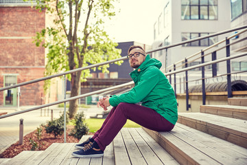 happy young hipster man sitting on stairs in city
