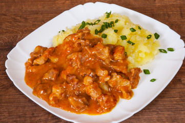 meat in sauce with mashed potatoes in a plate on wooden table