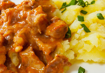 meat in sauce with mashed potatoes in a plate on wooden table