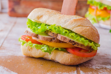Sandwich with roasted chicken, leaves salad and tomatoes on wooden baskgraund. Selective focus