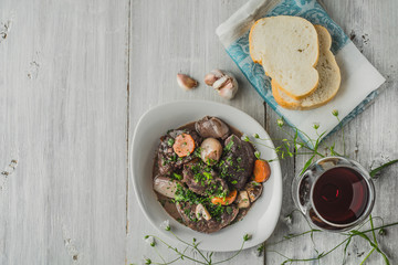 Beef bourguignon in a white ceramic plate with flowers and glass
