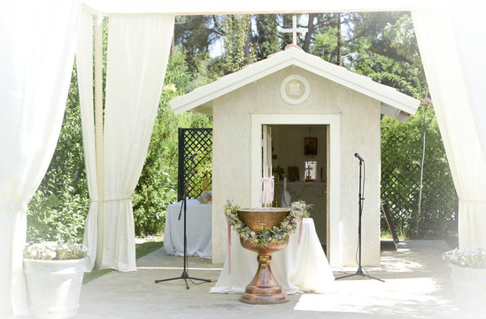 white tent  for wedding or entertainment events  with a very small chapel, and a baptism bowl, in a grass field on a sunny summer's day