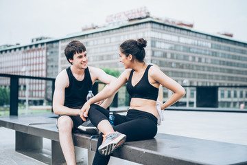 Fototapeta na wymiar Couple of young handsome caucasian sportive man and woman having a break after training, drinking water and drying themselves with a towel, chatting - sportive, fitness, health concept