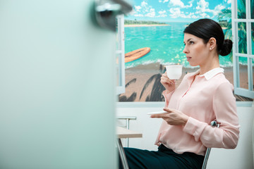 Woman resting with cup of in office kitchen.