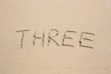 The numbers three written in the sand.