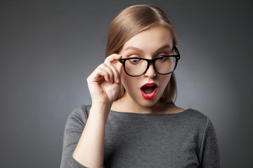 Wide-eyed woman in glasses looking down in amazement