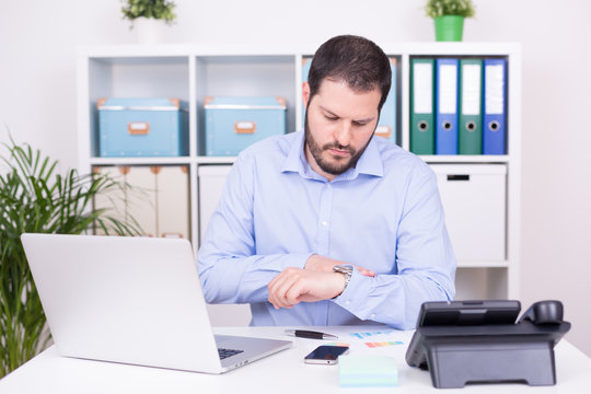 Gesch&auml;ftsmann im B&uuml;ro blickt auf Uhr