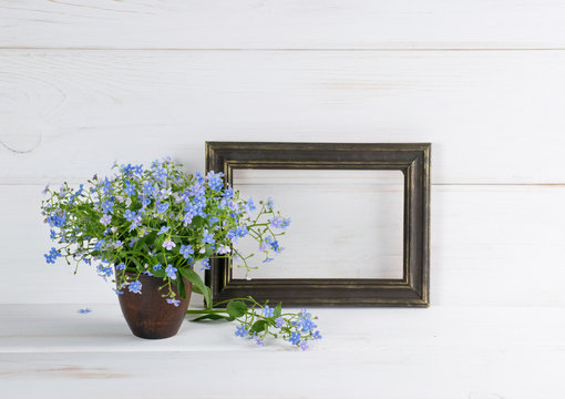 Forget-me-not flowers bouquet in clay vase and gilding photo frame on white wooden shabby board