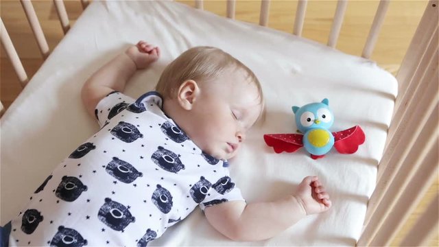 Baby sleeping with a toy owlet in a bedroom. One year old boy sleeping in his bed on the white sheet. Day child sleep