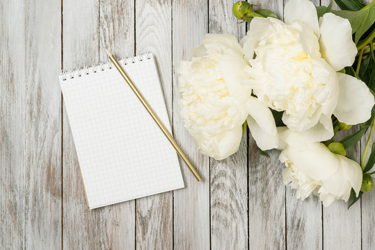 White peonies flowers with notebook and pencil on white painted wooden planks. Place for text. Top view.