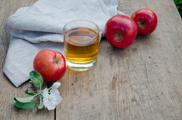 Apple juice and apples (red and green) on a wooden table with a gray tablecloth