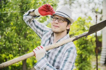 a young male farmer holding a shovel and smiling in the garden