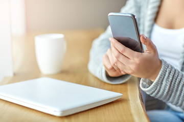 Woman holding a phone in hands and writes the message at the cafe. Close up