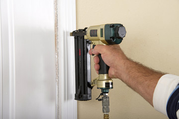 Do it yourself home owner repairing door frame molding with nail gun, close up on hand and nail gun.
